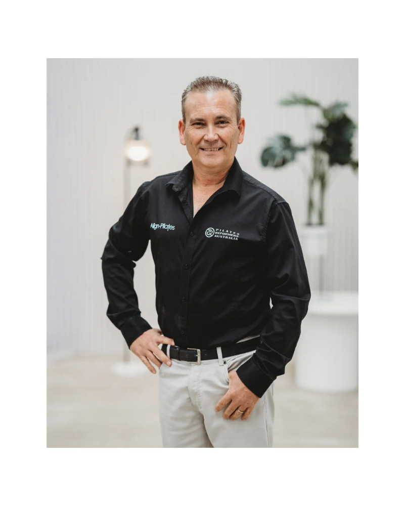 Pilates Reformers Australia CEO wearing a black shirt with logos in an indoor setting