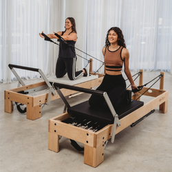 Two women using Pilates reformers in a studio setting.