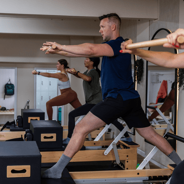 Group of people exercising on Pilates reformers in a studio.