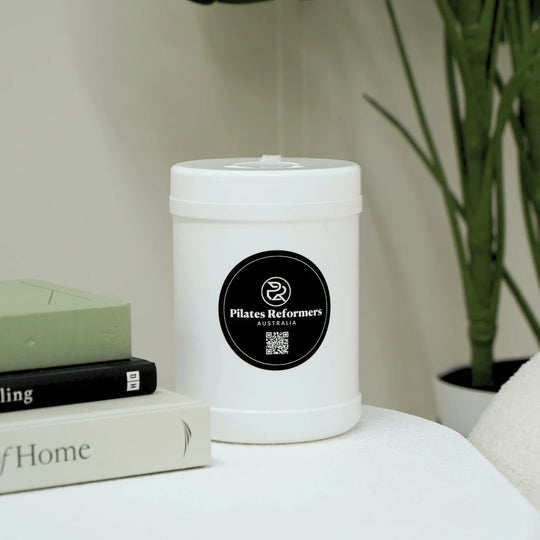 White wipe cannister with a label on a surface next to books and a plant