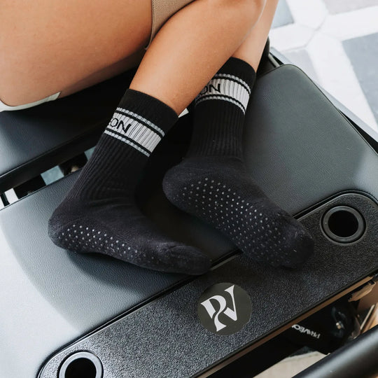 Black grip socks with white stripes and a visible brand logo, worn on a person's feet resting on a dark textured surface.