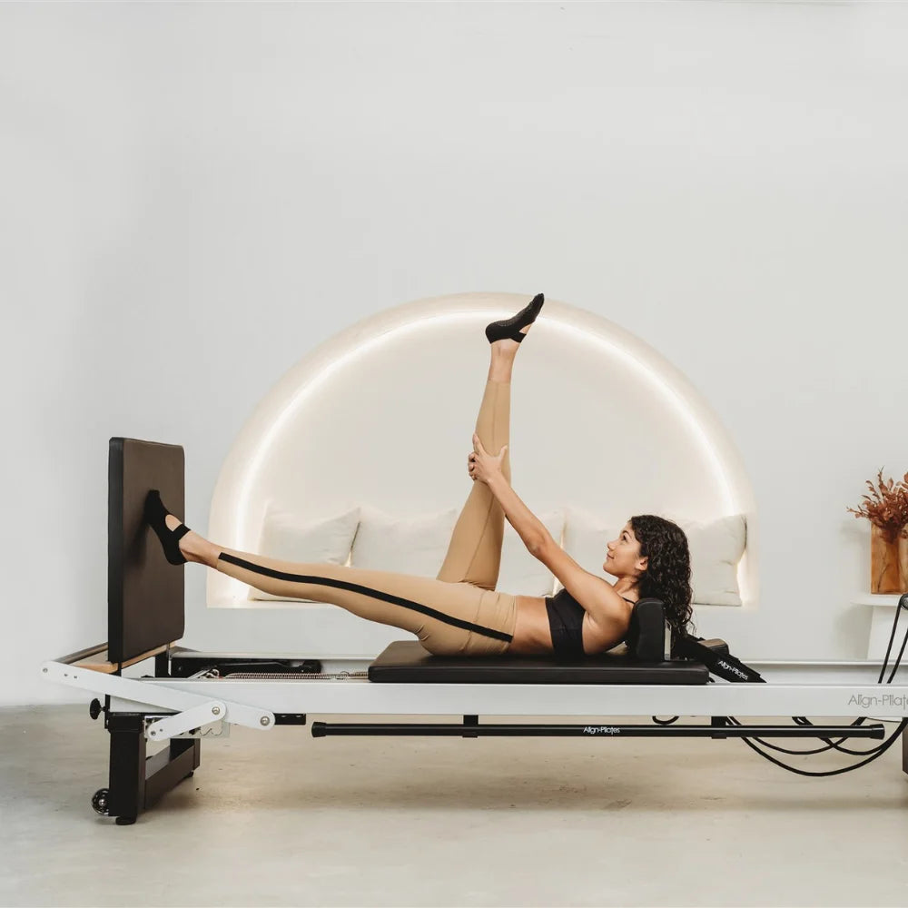 Woman doing leg extension on a white Pilates reformer