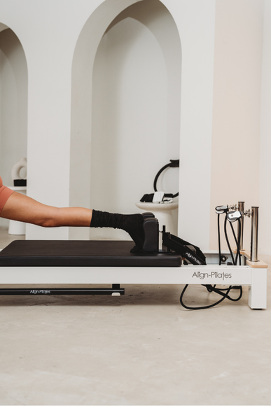 Person using a Pilates reformer machine in a minimalistic room with arches.