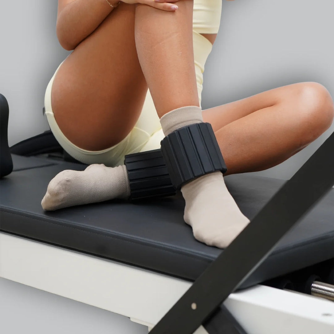 Person sitting on Reformer machine with black ankle weights