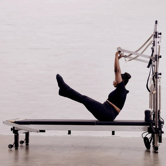 Person using a Pilates reformer machine with half trapeze in a studio setting.