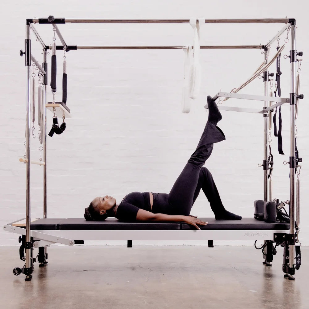 Person using a Pilates reformer with Cadillac in a studio setting.