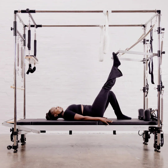 Person using a Pilates reformer with Cadillac in a studio setting.