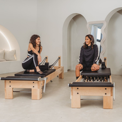 Two women on Pilates reformers in a studio setting