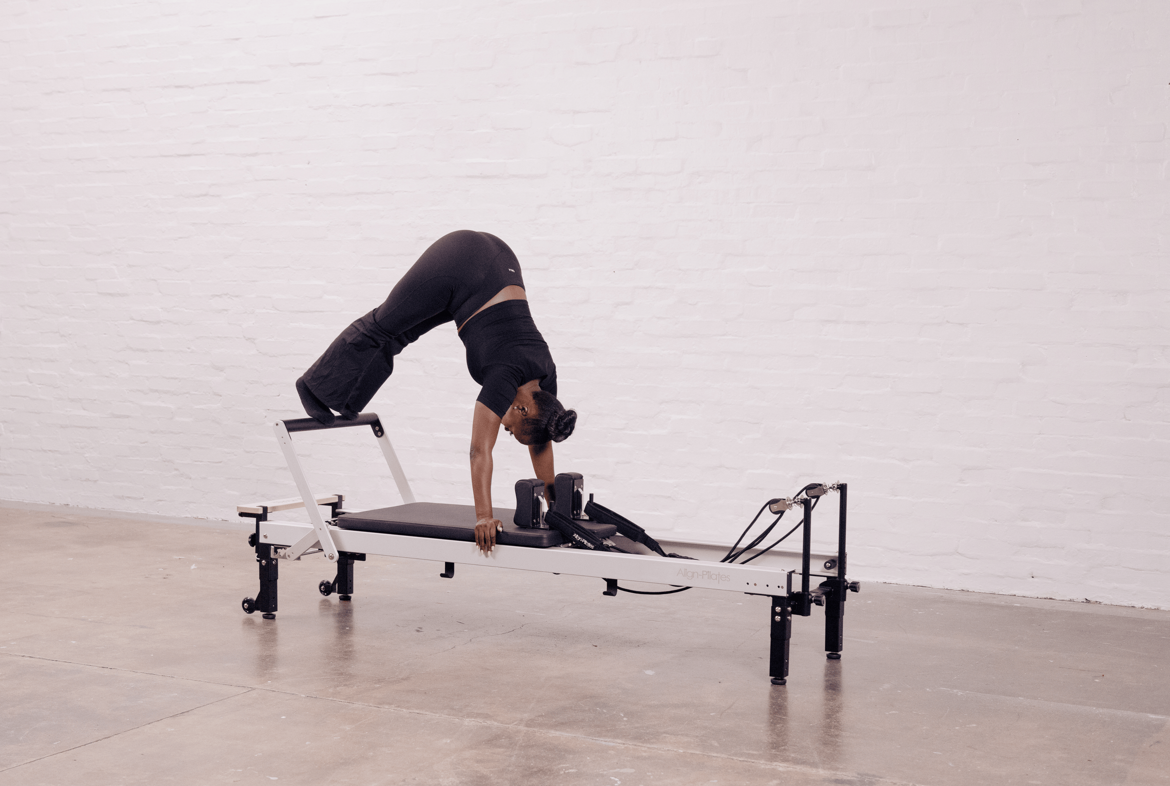Person using a reformer machine against a white wall