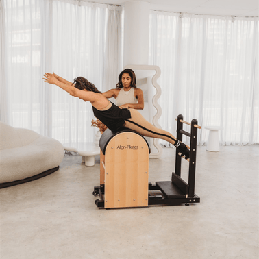 Woman using a Pilates Ladder Barrel in a bright room with white curtains.