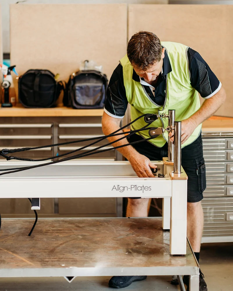 Person assembling a Pilates reformer machine in a workshop setting