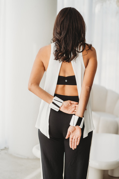 Person wearing a black sports bra and leggings with a white cardigan in a minimal indoor setting.